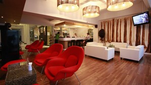 A modern lobby with red chairs, a white sofa, and a bar area. - The Embassy Sathorn (Bangkok)