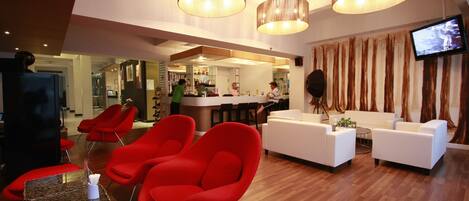 A modern lobby with red chairs, a white sofa, and a bar area.