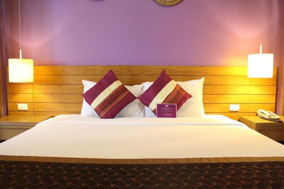 A hotel room with a large bed, two nightstands, a telephone, and a wall-mounted lamp.