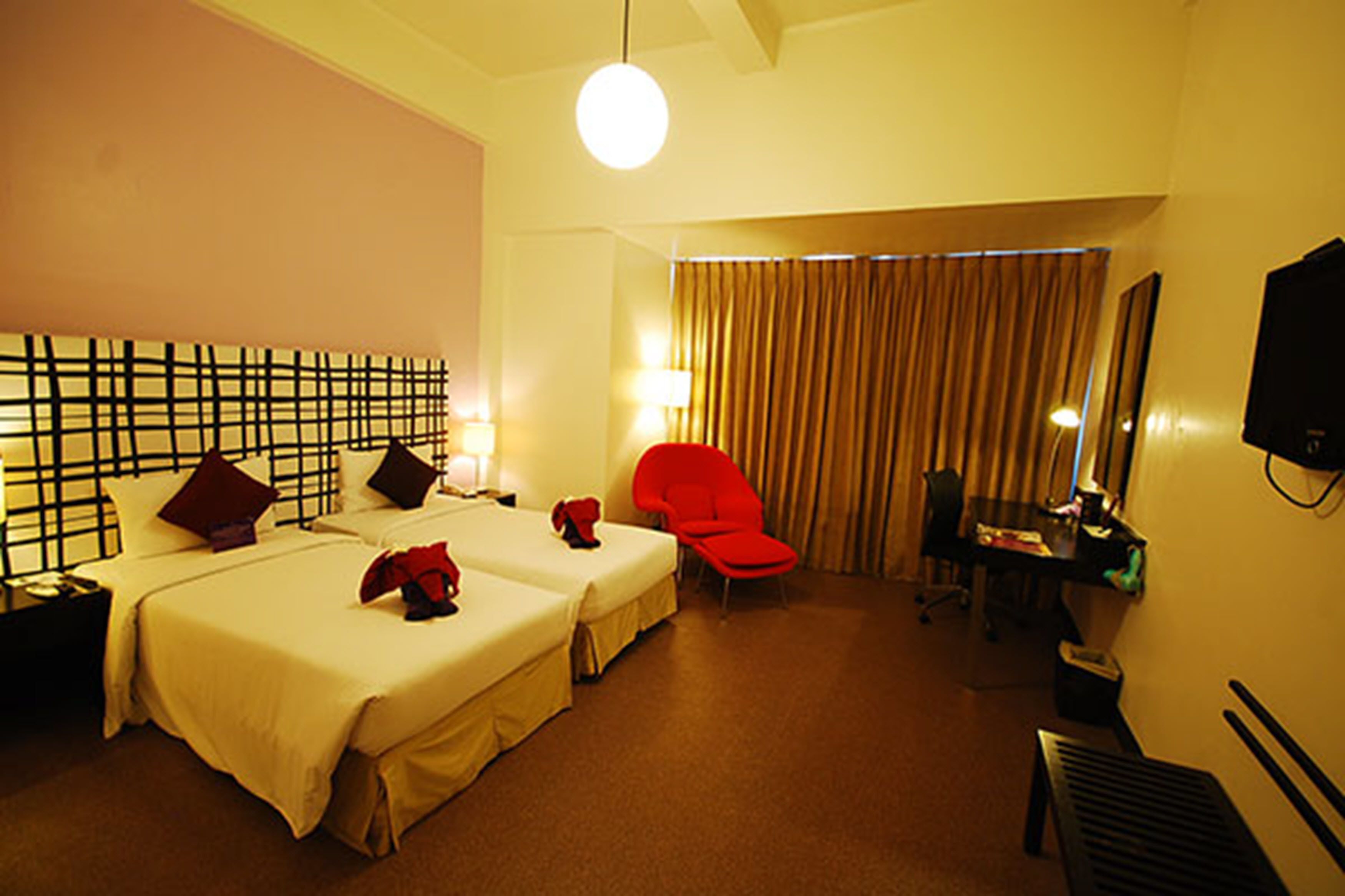 Ein Hotelzimmer mit zwei Betten, einem roten Sessel, einem Schreibtisch mit Computer und einem Fernseher.