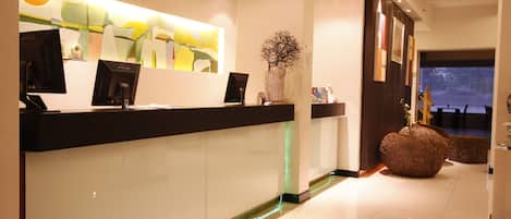 A reception area with a modern design, featuring a reception desk, a large abstract painting, and a decorative vase.
