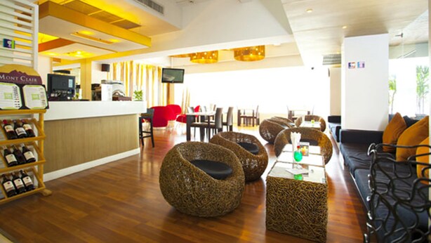 A modern hotel lobby with a wooden floor, wicker furniture, a reception desk, and a television screen. - The Embassy Sathorn (Bangkok)