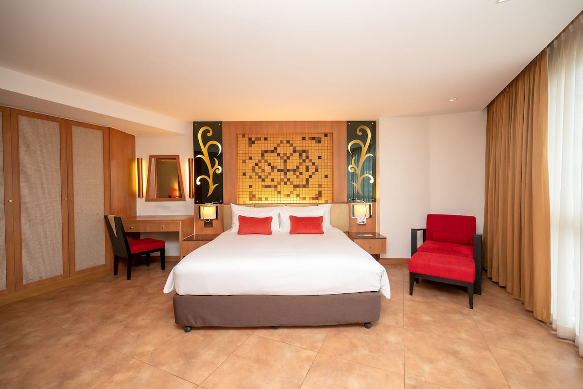 Una habitación de hotel con una cama grande, un escritorio, dos sillas, un armario y un panel decorativo en la pared.