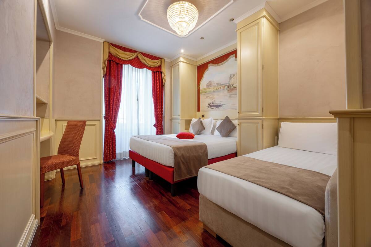 Habitación de hotel con dos camas, suelo de madera, una silla roja y un candelabro.