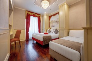 A hotel room with two beds, a wooden floor, a chandelier, and a painting on the wall.