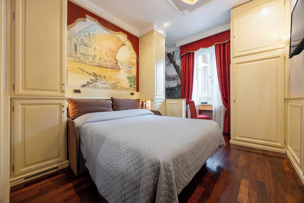 Un dormitorio con una cama grande, un cuadro en la pared y una ventana con cortinas rojas.