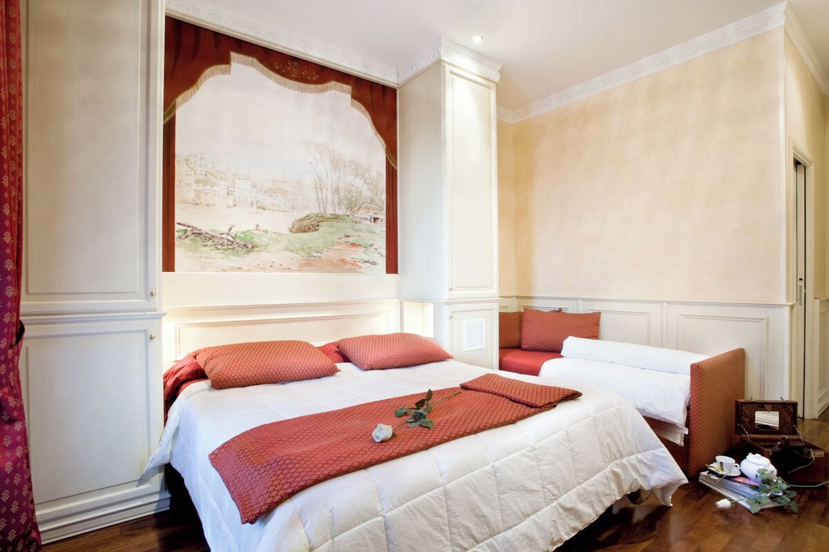 A hotel room with a large bed, two pillows, a bedside table, and a painting on the wall.
