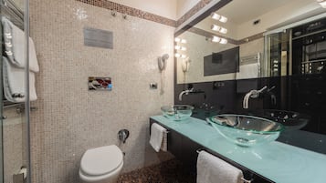 A modern bathroom with a glass sink, a toilet, and a large mirror.