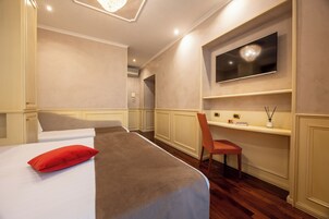 Una camera d'albergo con un letto, una televisione montata a parete, una poltrona e un tavolino con un vaso.