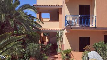 A multi-story building with a central courtyard, featuring a stone pathway, various potted plants, and a blue balcony railing.