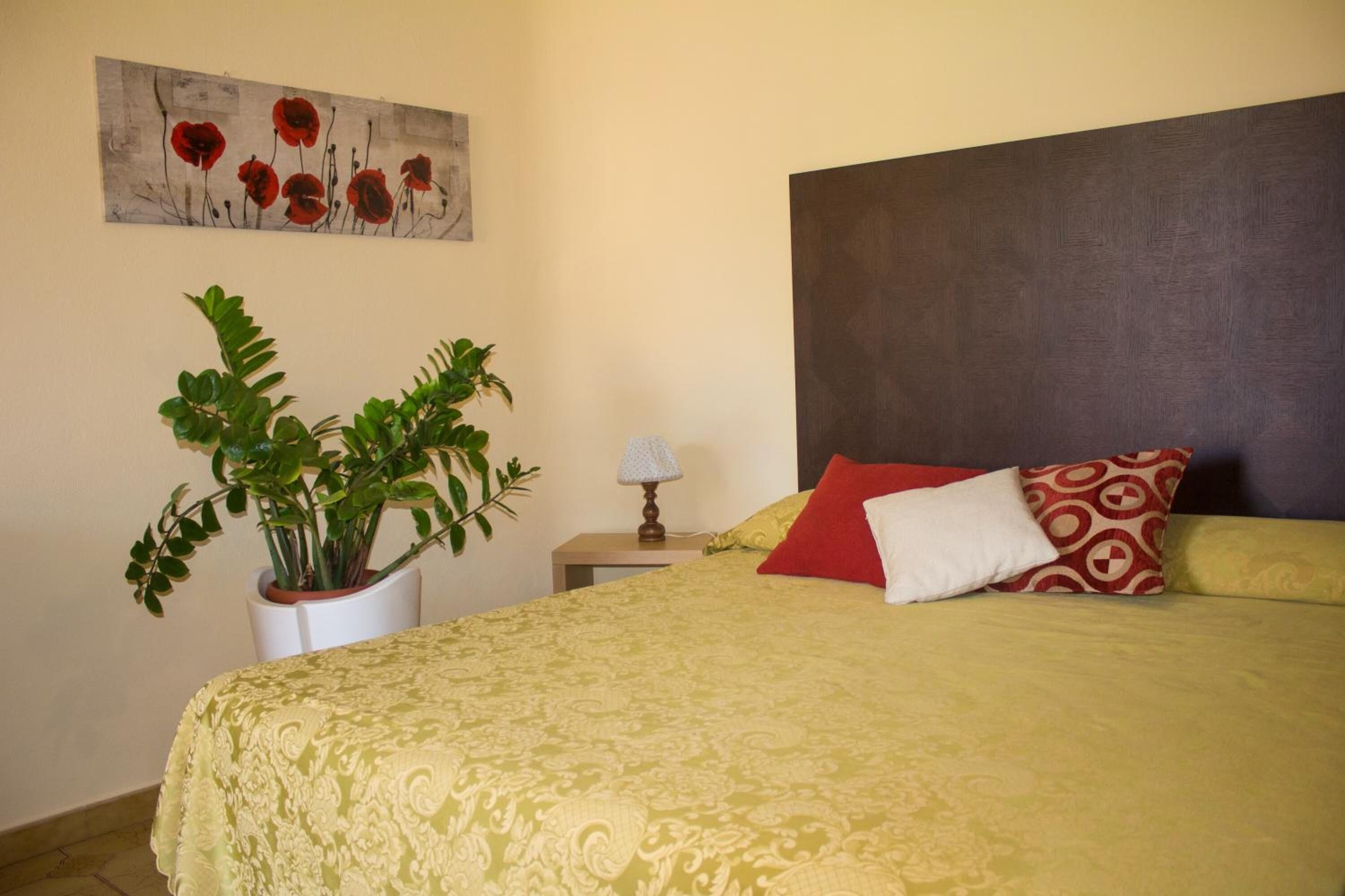 Une chambre à coucher bien rangée, avec un grand lit, une plante en pot, une table de chevet avec une lampe et un tableau accroché au mur.