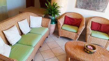 Una habitación con muebles de mimbre, incluyendo un sofá y dos sillones con cojines, una mesita y una planta en maceta.