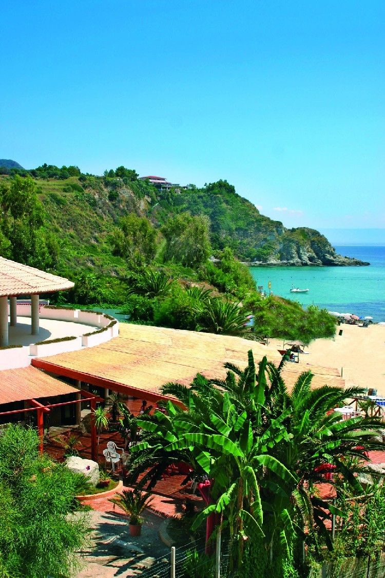 A beach resort with a patio area, a view of the sea, and lush greenery.