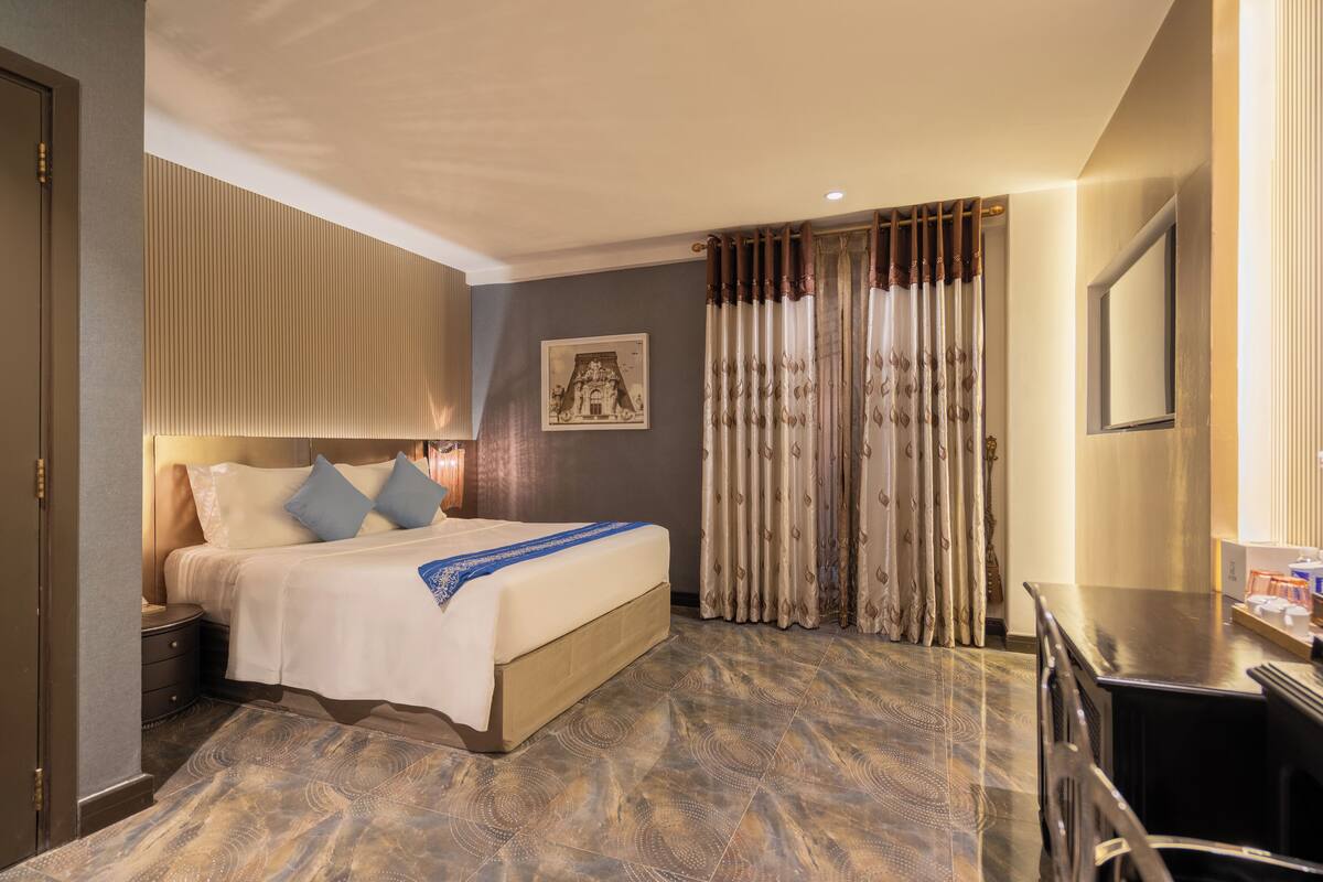 Ein Hotelzimmer mit Bett, Nachttisch, Vorhängen und einem an der Wand befestigten Fernseher.