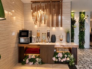 A modern reception area with a coffee machine, a TV, and a decorative wall with vertical wooden slats and greenery. - A&EM Ben Thanh Hotel (Ho Chi Minh City)
