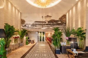 Un hall d’hôtel avec un couloir central, un comptoir d’accueil et une fresque murale.