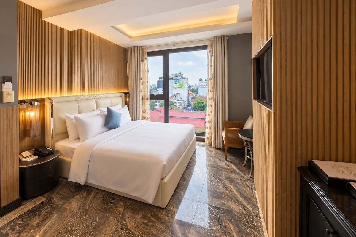 Een hotelkamer met een groot bed, een bureau, een stoel, een televisie en uitzicht op de stad.