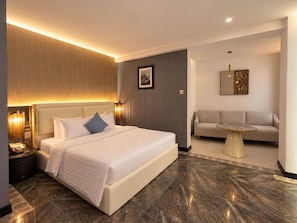 Een moderne hotelkamer met een groot bed, een slaapbank, een klein rond tafeltje en een wanddecoratie.