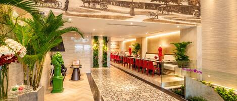 A hotel lobby with a long reception desk, red chairs, a massage spa area, and a mural depicting a historical scene.