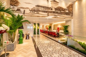 Un hall d’hôtel doté d’un long comptoir d’accueil, de fauteuils rouges, d’un espace dédié aux massages et d’une fresque représentant une scène historique.
