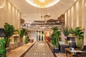 A hotel lobby with a central corridor, decorative plants, a reception desk, and a mural on the wall. - A&EM Ben Thanh Hotel (Ho Chi Minh City)
