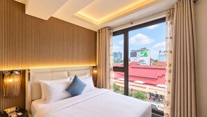 Een hotelkamer met een groot bed, een nachtkastje, een lamp en uitzicht op de stad.
