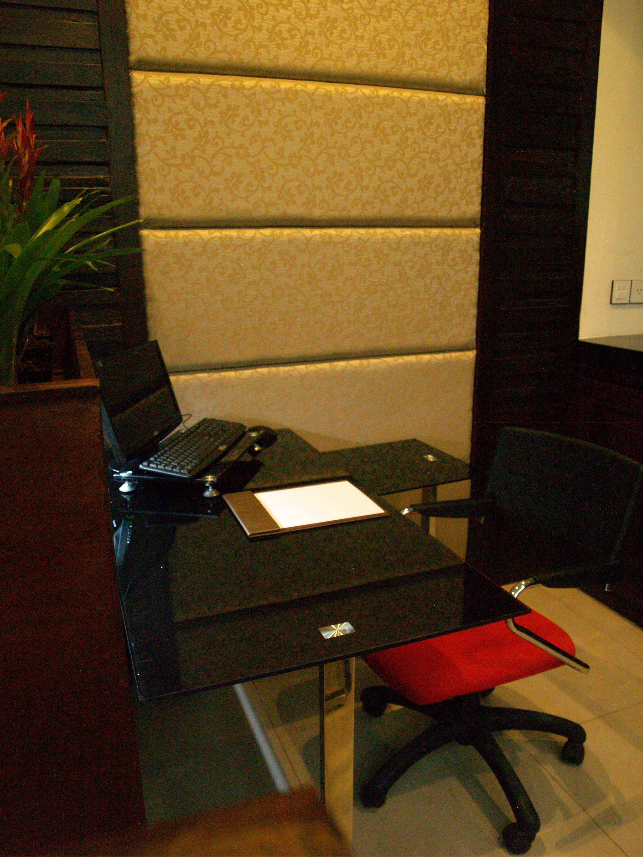 A modern office space with a glass desk, a laptop, a red cushioned chair, and a potted plant.