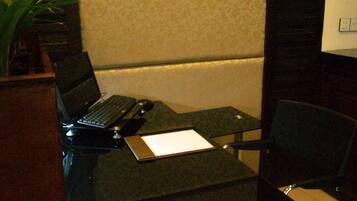 A modern office space with a glass desk, a laptop, a red cushioned chair, and a potted plant.