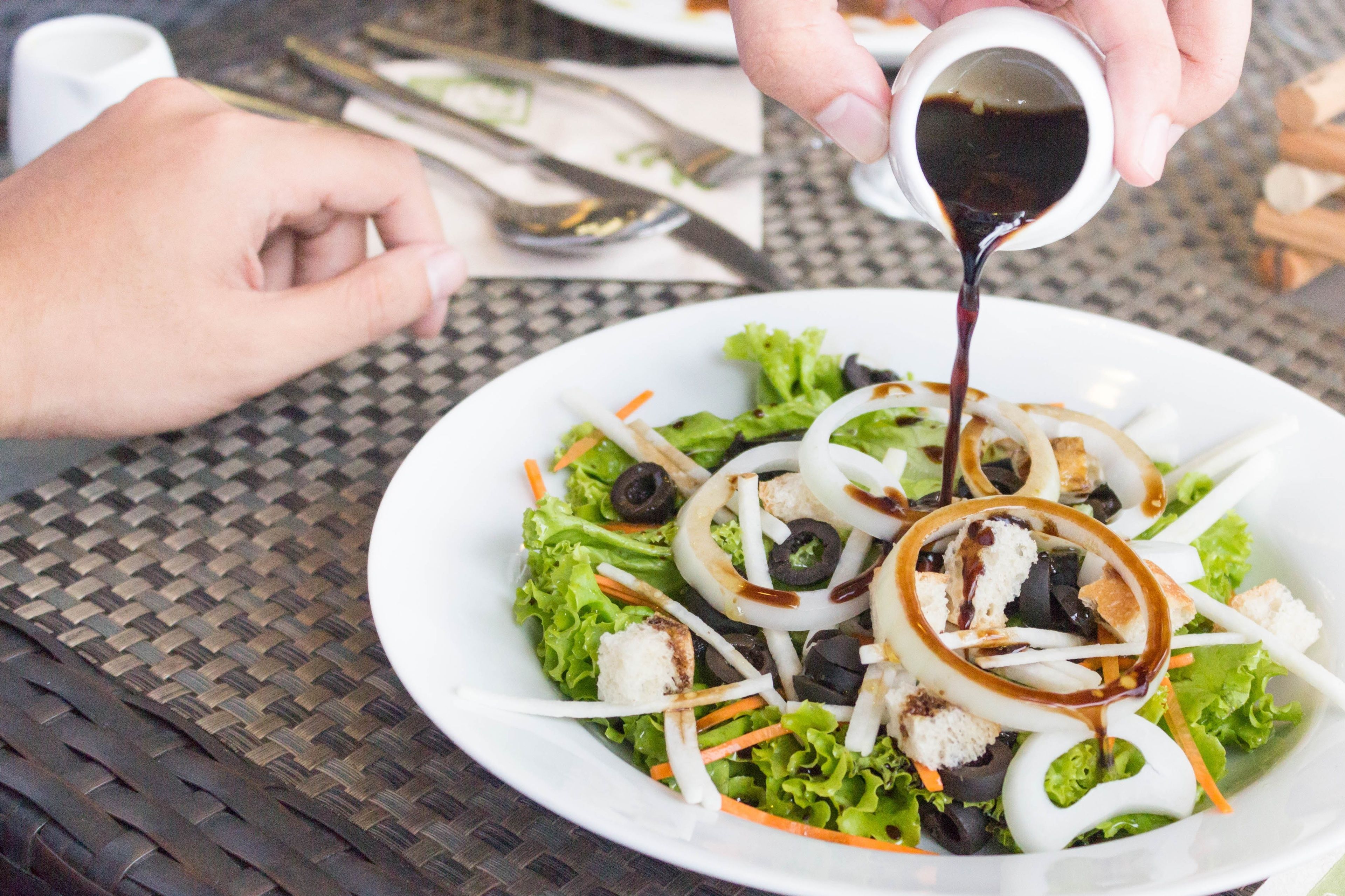 A person pouring a dark sauce over a salad with lettuce, carrots, and croutons.
