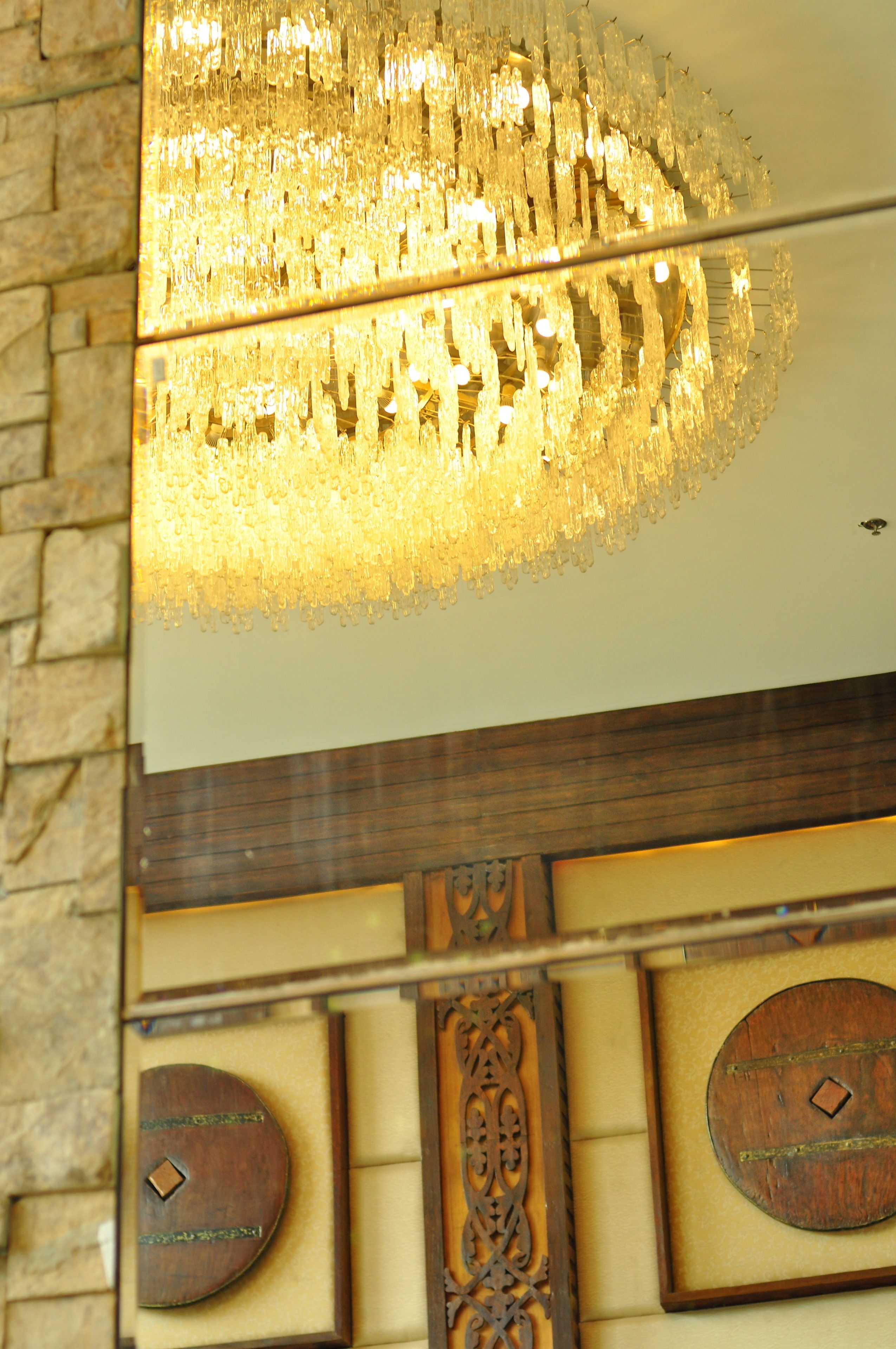 Um candelabro com superfície refletora, um painel de madeira com detalhes entalhados e um emblema circular na parede.