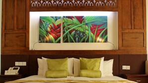 A hotel room with a large bed, green and white pillows, a wooden headboard, and a painting of tropical plants above the bed. - Cocoon Boutique Hotel (Quezon City)