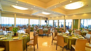 A spacious dining area with multiple round tables set for dining, large windows offering a view, and a chandelier hanging from the ceiling. - Cocoon Boutique Hotel (Quezon City)