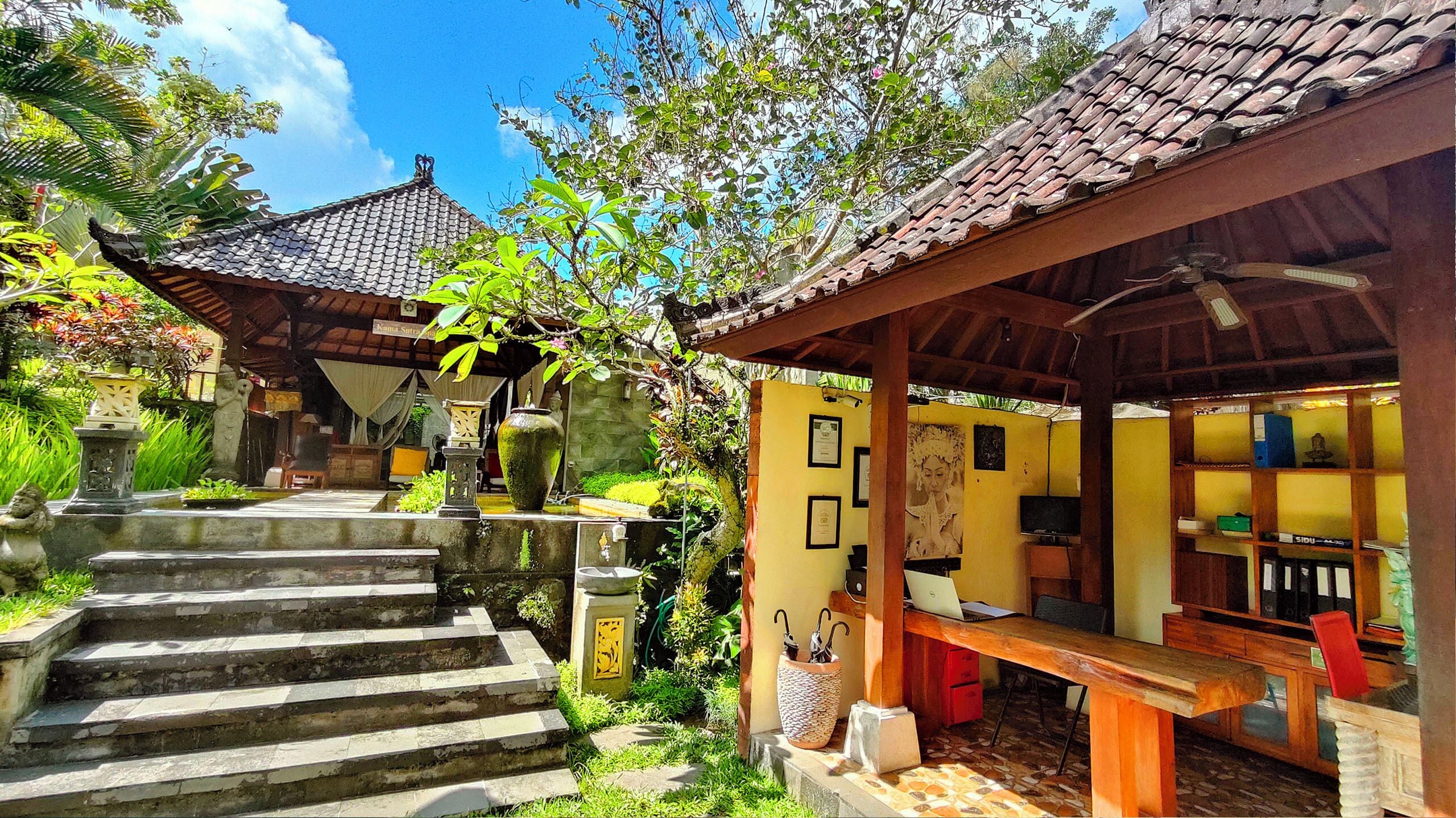 Een traditioneel Balinese huis met een pannendak, een houten veranda en een stenen trap naar een deur.