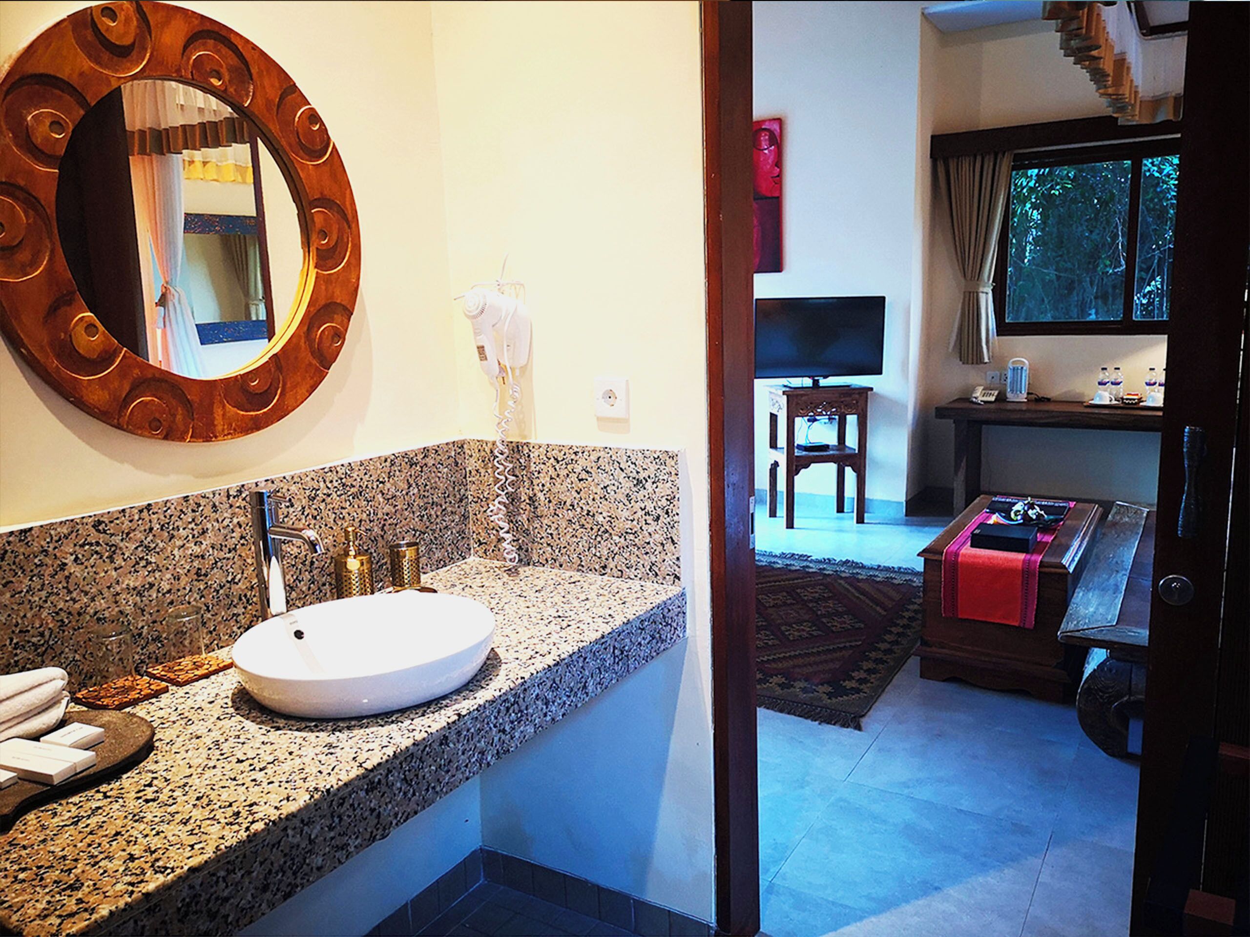 A bathroom with a granite countertop, a round mirror, and a white sink.