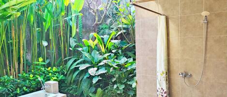 A modern bathroom with a bathtub, shower, and a view of lush greenery.