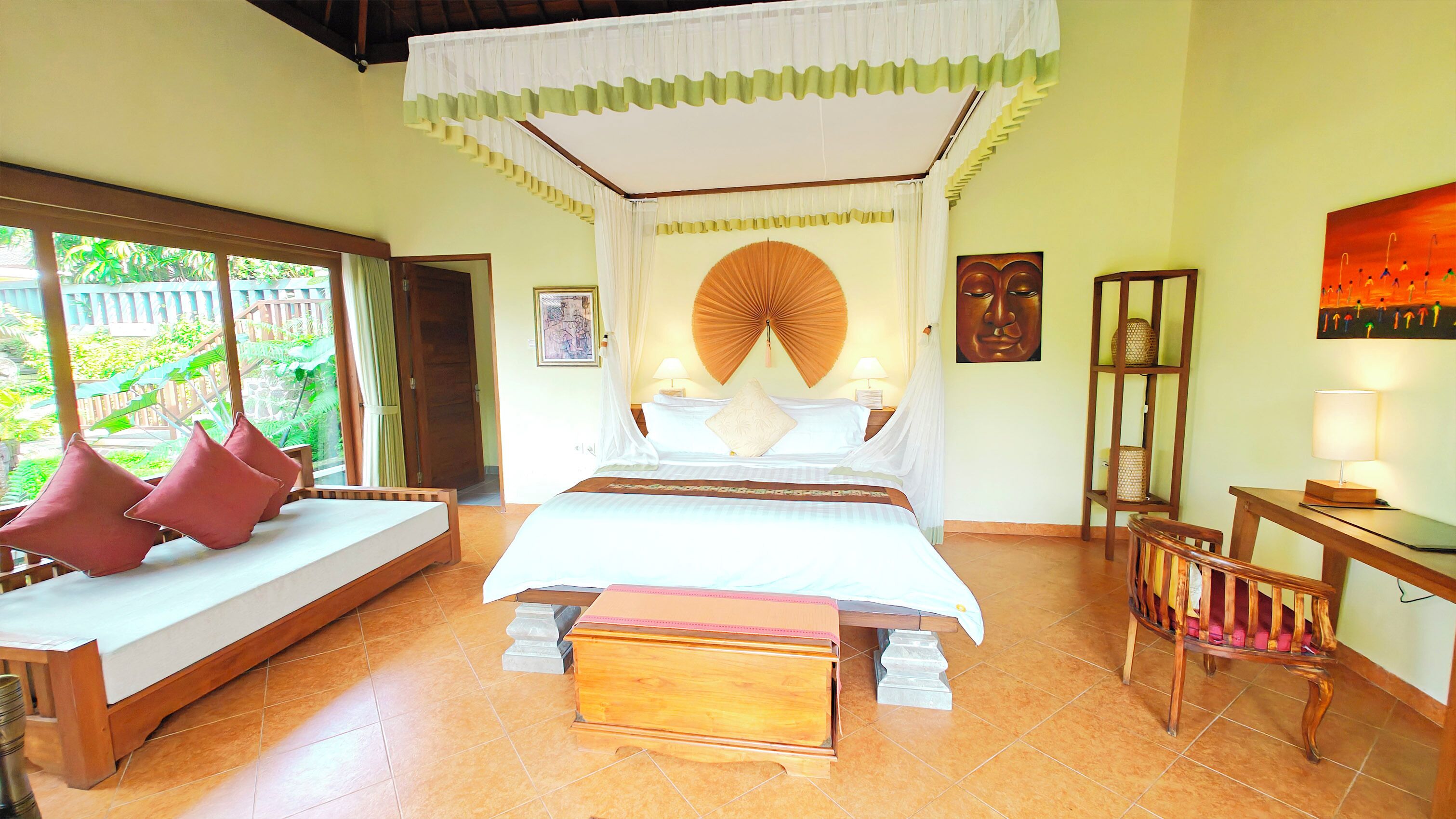 A room with a bed, a bench with cushions, a table with a lamp, and a painting on the wall.