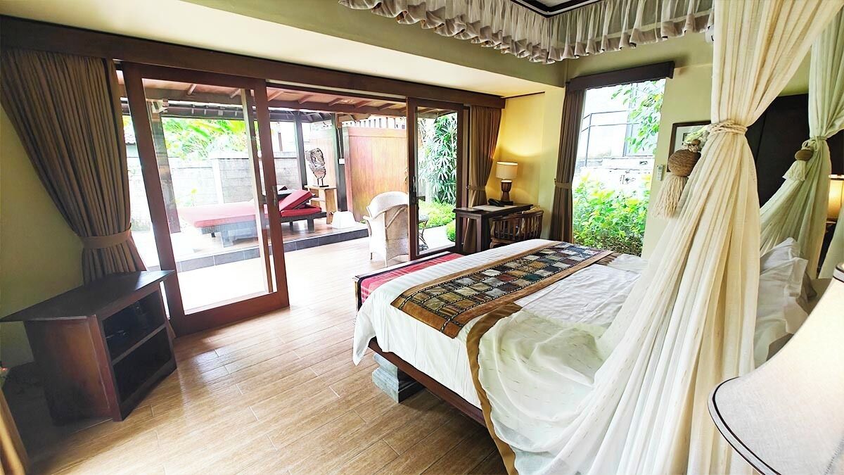 Un dormitorio con cama, mesita de noche, lámpara y vistas al exterior.