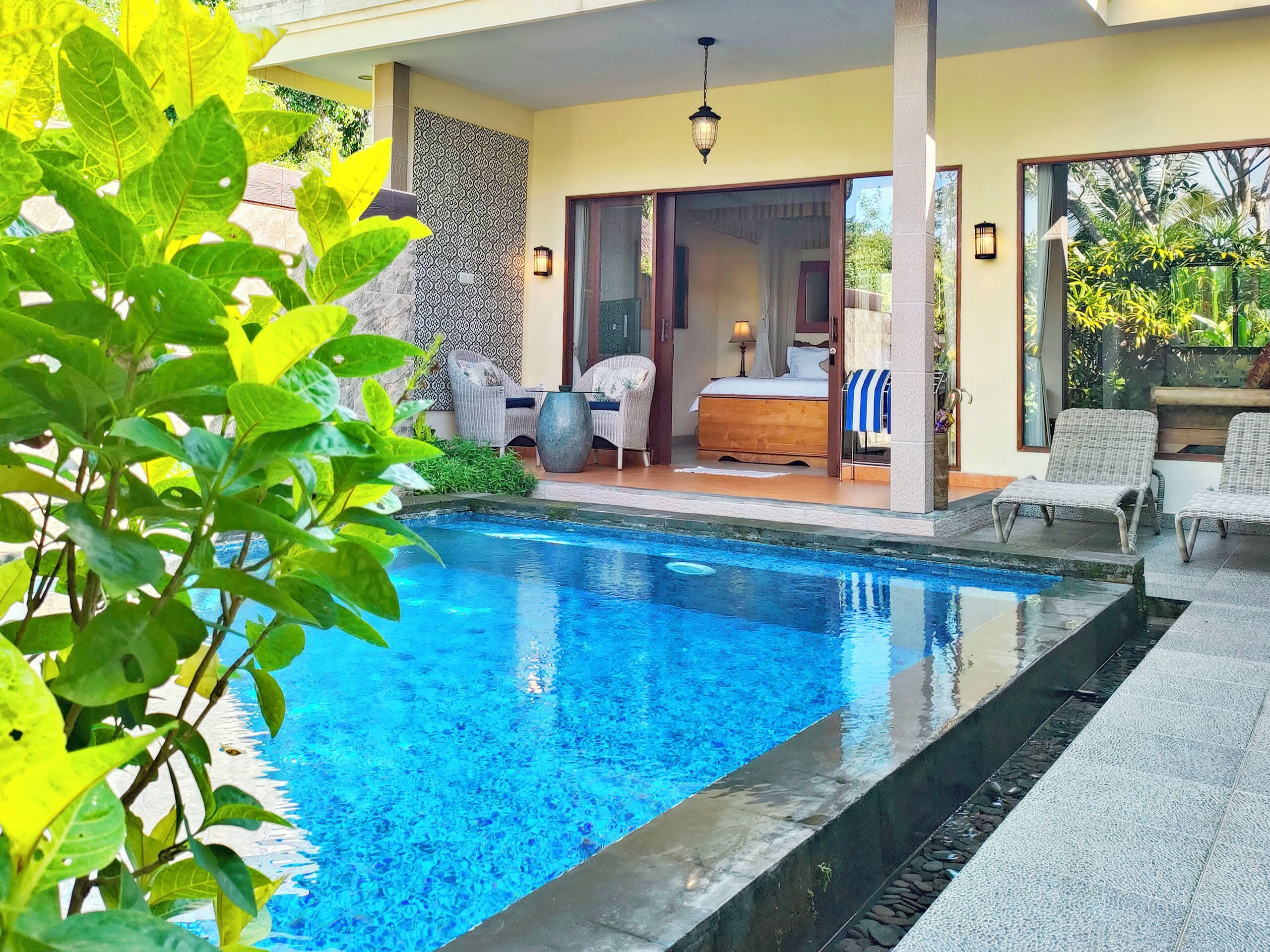 A poolside bedroom with a bed, a chair, and a view of the pool.