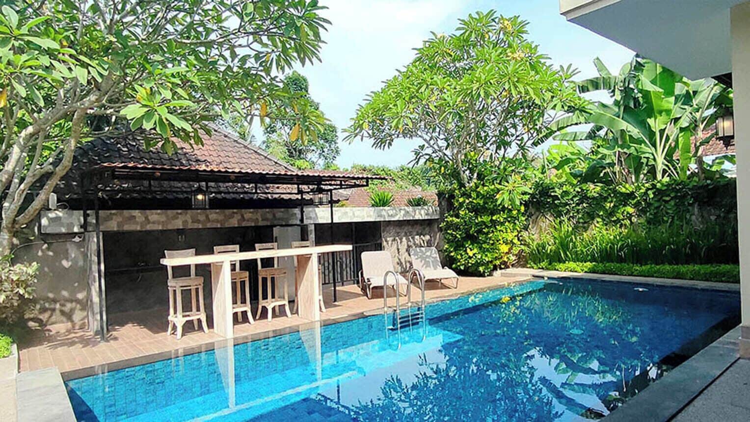A swimming pool with a stone structure and seating area, surrounded by lush greenery.