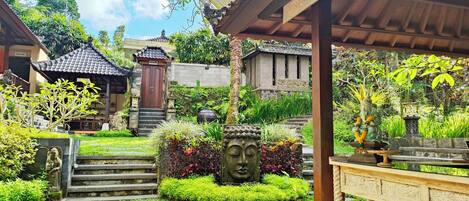 A traditional courtyard with stone steps leading to a wooden door labeled "Reception & Cashier," surrounded by lush greenery and a stone statue.