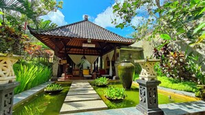 Un edificio tradicional japonés con tejado de tejas, rodeado de exuberante vegetación y un pequeño estanque con plantas.