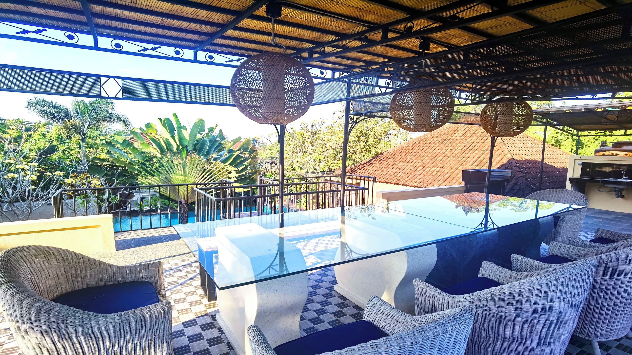 A glass-top dining table with wicker chairs, a pool, and a view of a red-roofed building.
