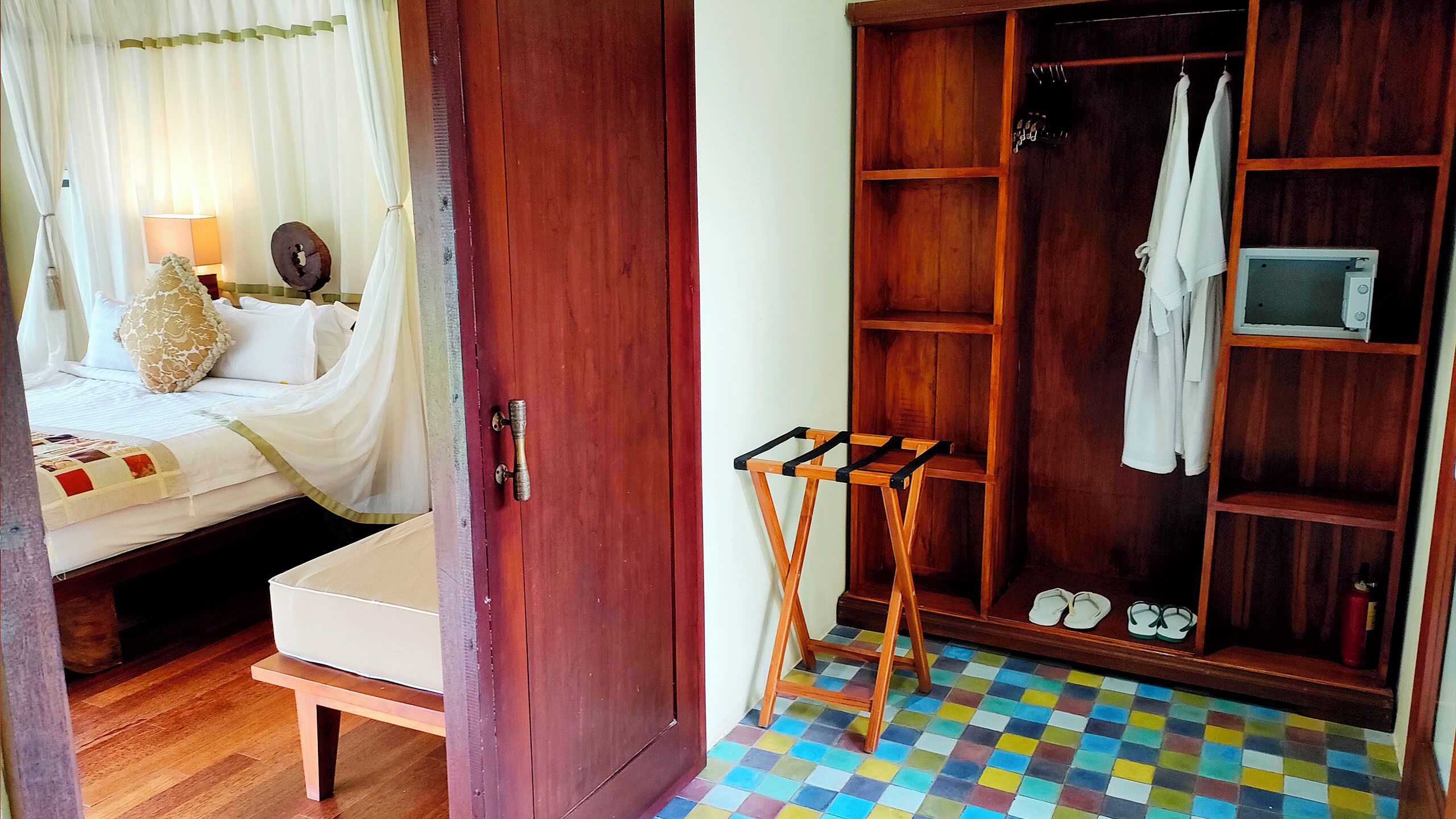 A bedroom with a bed, a bedside table, a wooden wardrobe, and a small stool.