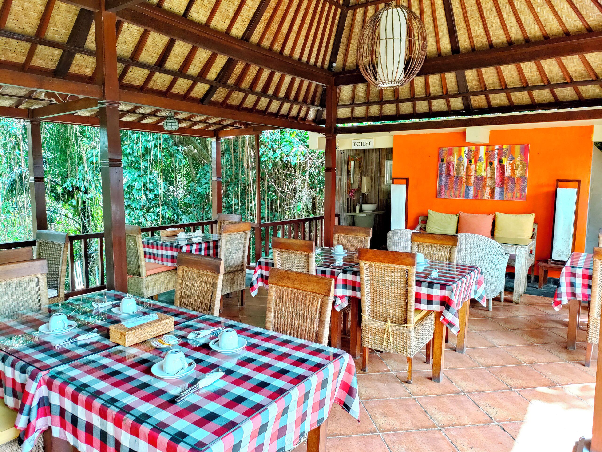 A covered outdoor dining area with checkered tablecloths, wicker chairs, and a tiled floor.