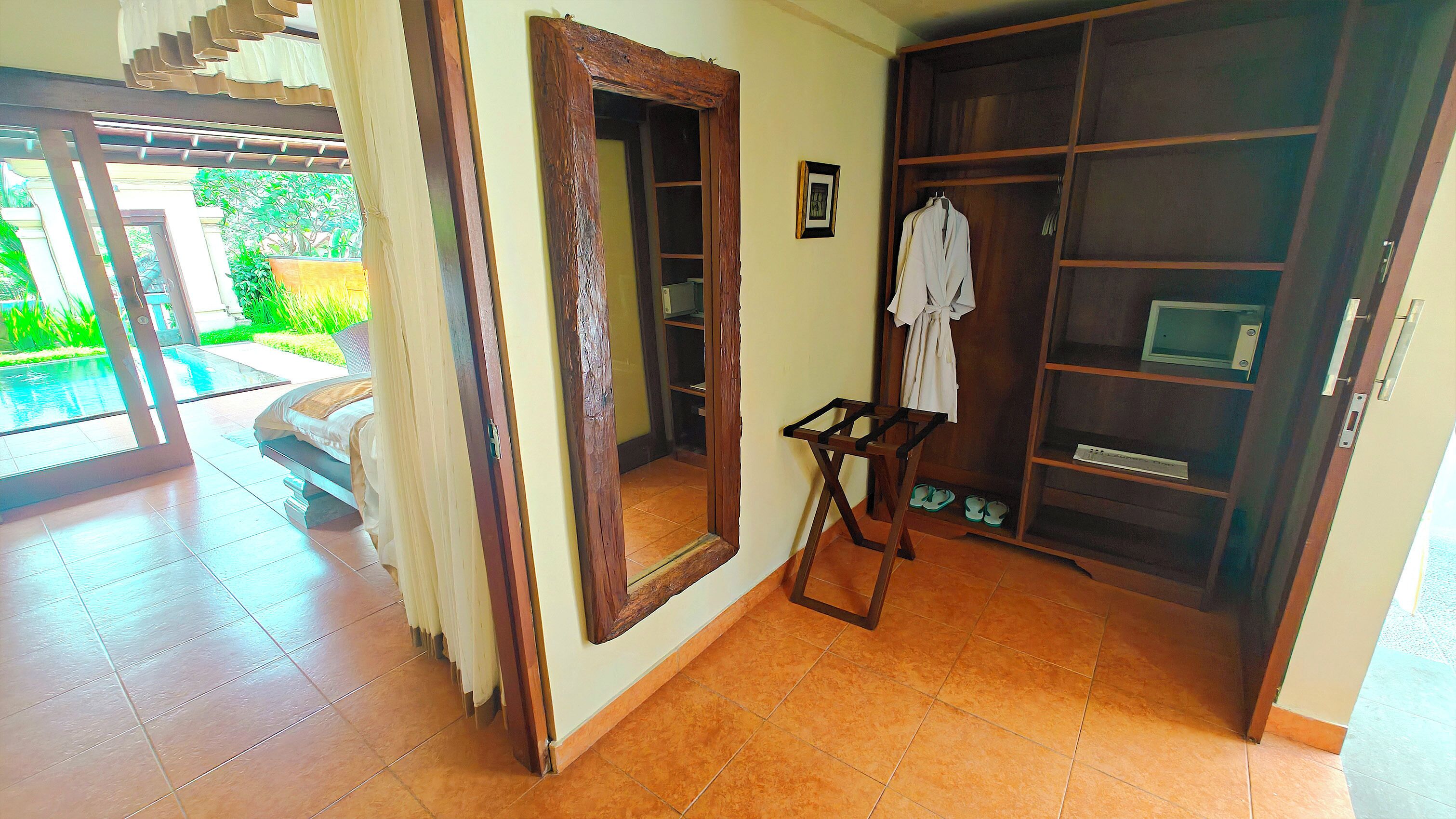 A room with a large wooden wardrobe, a small table with a chair, and a view of a swimming pool through a glass door.