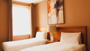 Una habitación de hotel con dos camas, una mesita de noche con lámpara y un cuadro en la pared.