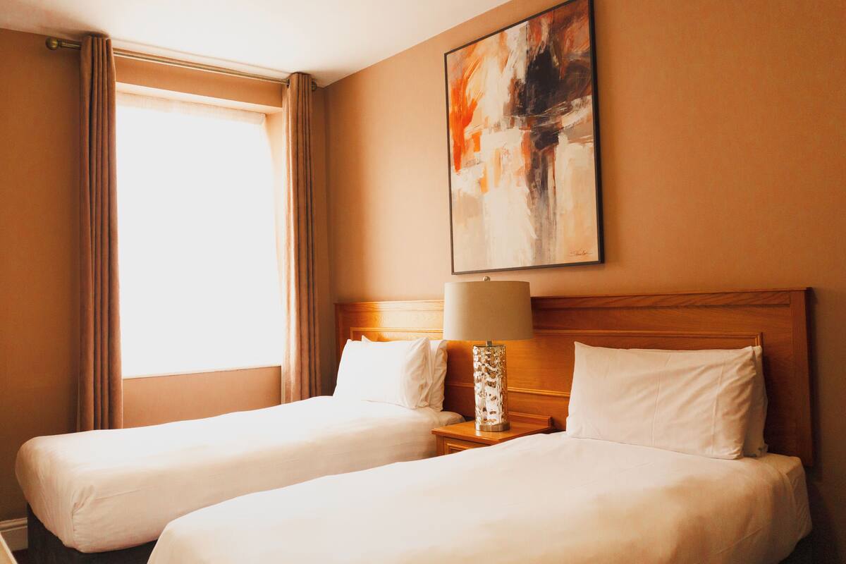 A hotel room with two beds, a nightstand with a lamp, and a painting on the wall.
