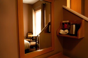 Habitación de hotel con un espejo de marco de madera que refleja un área de comedor con una mesa y sillas. Se ve una repisa con una cafetera y tazas.