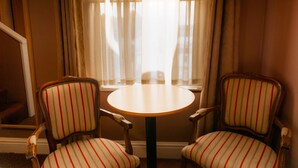 Una habitación con dos sillas a rayas alrededor de una pequeña mesa redonda, un espejo y una ventana con cortinas.
