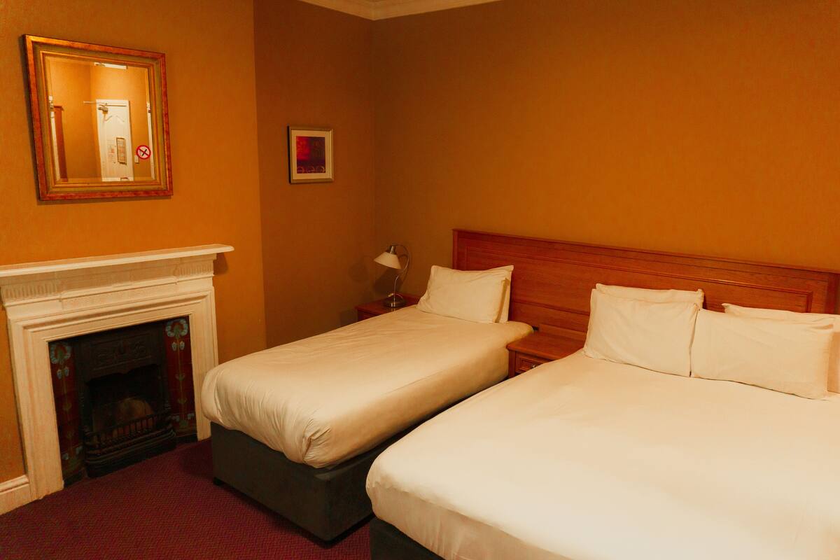 A hotel room with two beds, a fireplace, and a nightstand with a lamp.